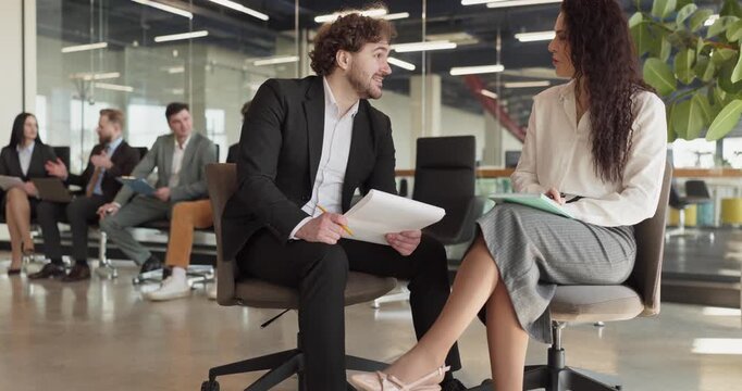 Business colleagues, man and woman, in office discussion. Seated with papers, they prepare for a meeting or seminar in a modern workspace together. Concept shows clear teamwork values.