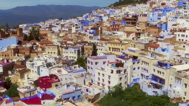 Low drone pan skims Chefchaouen rooftops revealing laundry, facades, and Rif.