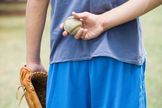 Mid section view of a teenage boy hiding a baseball behind his back