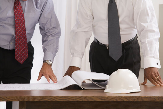 Mid section view of two engineers looking at a blueprint in an office