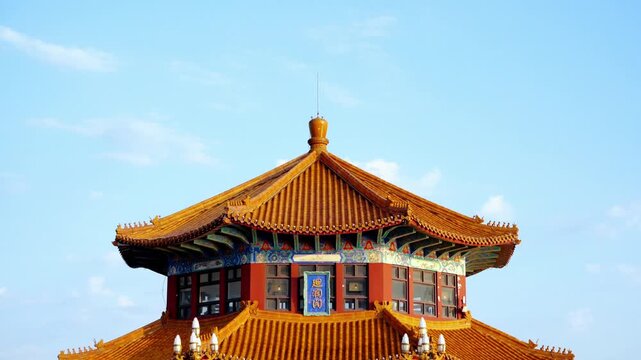 A double-eaved traditional Chinese pavilion with golden glazed tile roofs and red walls, set against a clear blue sky on a sunny day.