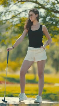 Model poses outdoors in sportswear with golf club on sunny day at the park