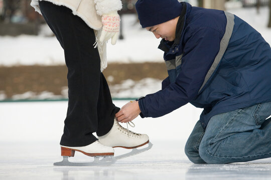Young man tying ice skate laces of a young woman