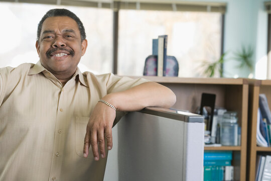 Man standing in his workplace, leaning on the wall of his cubicle wearing casual clothing