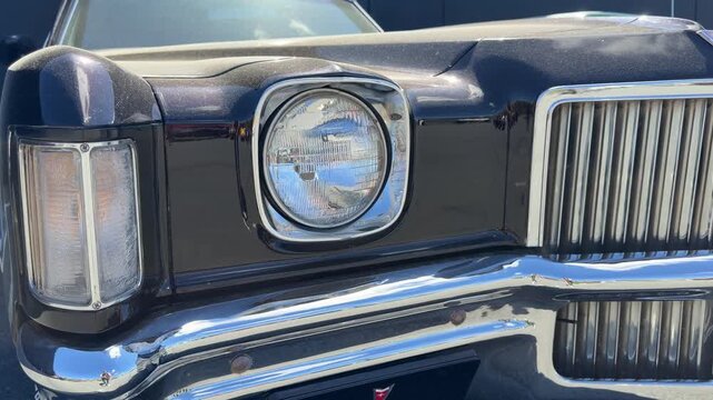 Classic car headlights glisten under the warm sunlight, highlighting their vintage charm and intricate designs at an auto showcase filled with nostalgia and history