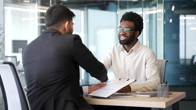 Employer sitting at desk shaking hands with job applicant after interview. HR director welcoming new employee on board, confirming hiring decision and successful recruitment in modern corporate office