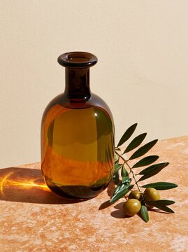 Close up of single dark glass bottle of premium olive oil with green olives and olive branch on a textured surface against a neutral background