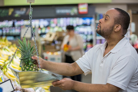 Man with Down Syndrome weighing pineapple in a grocery store