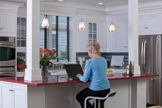 Woman on laptop in kitchen of a Green Technology Home with energy efficiency appliances, stone