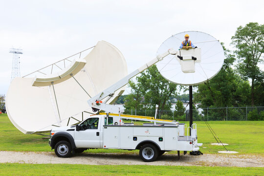 Communications engineer in bucket truck in front of satellite dish