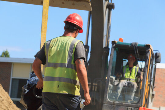 Construction engineer guiding water pipe suspended by excavator at construction site