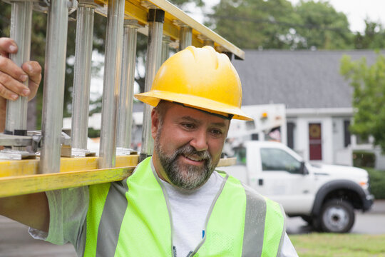 Utility worker carrying a ladder for work at site