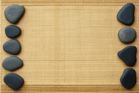 Spa background with black zen stones frame on bamboo mat texture with copy space