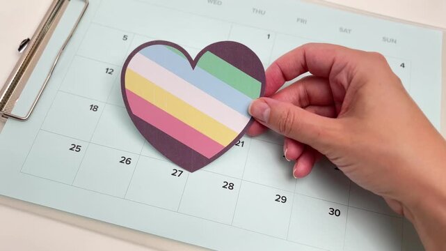 Hand placing a heart with the Disability Pride flag colors on a calendar, inclusivity and awareness concept