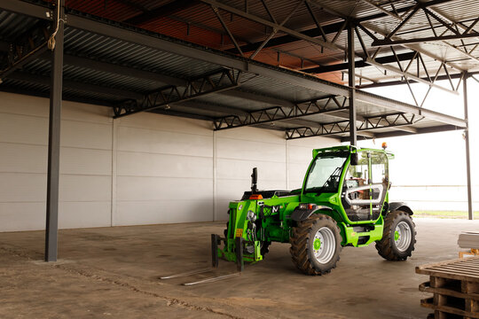 Green telehandler forklift truck parked inside empty industrial warehouse hanger, logistics distribution storage building facility with concrete floor and steel metal structure architecture constructi