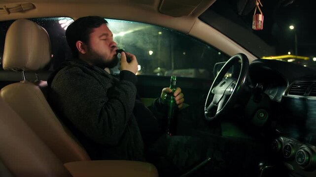 Bearded drunk adult man with bottle exhaling in breathalyzer inside vehicle at night. Person uses blood alcohol test in parked automobile with foggy windows during darkness and looks at the result