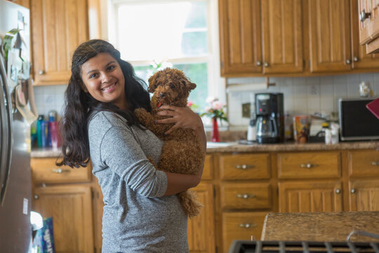 Woman with autism spectrum disorder standing in the kitchen holding her pet dog and looking at the