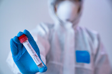 Obraz premium Scientist Holding Ebola Test Tube: A scientist in protective gear holds up an Ebola virus test tube, a symbol of medical research and the fight against infectious diseases.