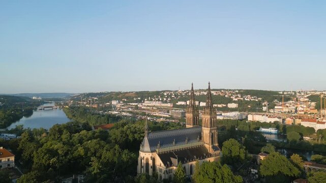 Witness the captivating beauty of Vysehrad Basilica of St. Peter and St. Paul in Prague during a serene sunrise. The vibrant colors illuminate the historic church and surrounding landscape.