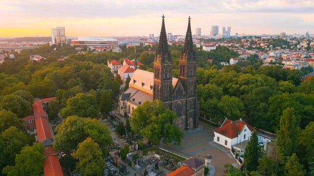 Witness the breathtaking Vysehrad Basilica of St. Peter and St. Paul glowing in the early morning sky. Explore the stunning architecture surrounded by nature and the city skyline.