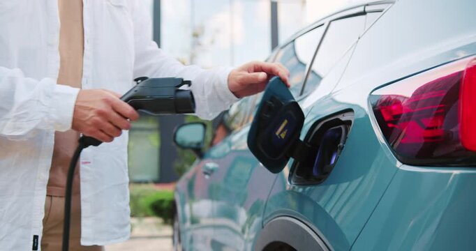 Close up of male hands plugging charger into electric car in the parking lot, outdoors