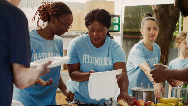 At outdoor food bank, multiethnic female volunteers provide free food to homeless men.