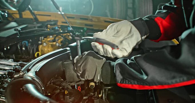 Slow motion shot of mechanic working on car engine with camera movement above engine, dramatic lighting in workshop. Automotive repair concept, maintenance and service.