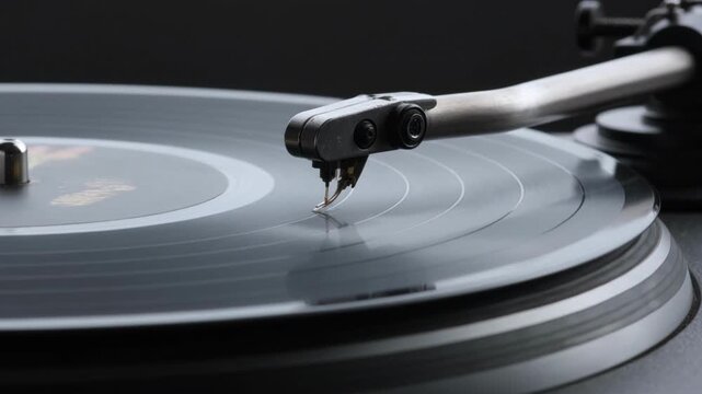 Cinematic close-up of a turntable stylus playing a black vinyl record. Vintage record player spinning in dark studio lighting. Retro music and nostalgic analog audio equipment concept.