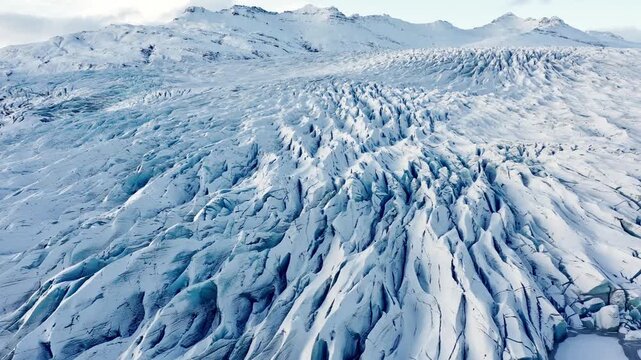 Expansive Aerial View of a Vast, Snow-Covered Glacier with Jagged Ice Formations and Mountains