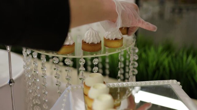 Waiter in gloves placing elegant meringue tartlets on a crystal glass stand