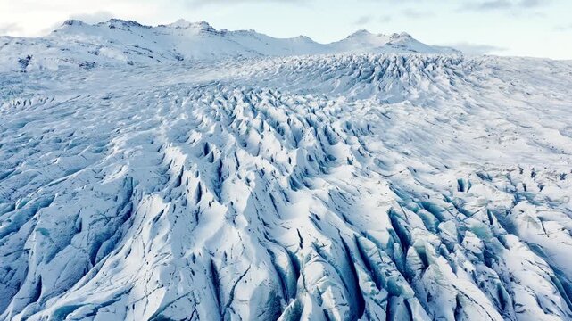 Expansive Aerial View of a Vast, Textured Glacier with Snow-Covered Mountains in the Background