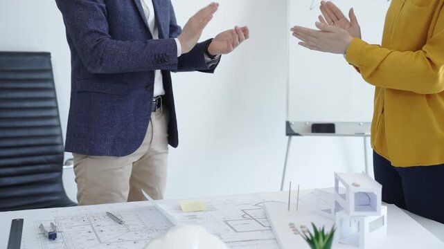 Business partners shaking hands over blueprints in an office, finalizing a construction project deal and confirming collaboration or a new architectural agreement