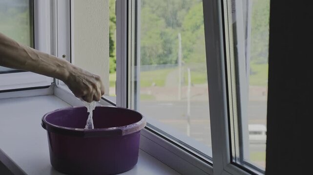 Daily routine of a woman cleaning the house. An arm with prominent veins squeezing water from a cleaning cloth into a bucket on a window sill