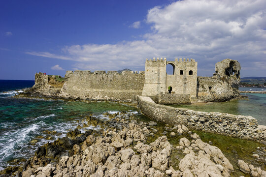 The Methoni Castle, a Venetian fortress on the coast of Greece, stands against a bright blue sky with scattered clouds.