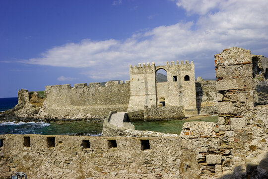 The Methoni Castle, a Venetian fortress on the coast of Greece, stands against a bright blue sky with scattered clouds.