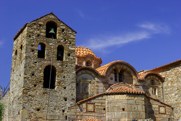 A bell tower and domes of a stone church under a blue sky. © Nick