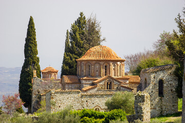 The Byzantine monastery of Hosios Loukas in Boeotia, Greece, with its distinctive terracotta tiled domes and stone architecture, surrounded by cypress trees and blooming vegetation under a clear sky. © Nick