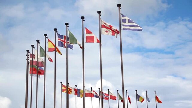 Row of national flags of various european countries waving on flagpoles against a cloudy blue sky