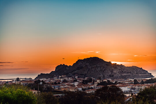 Silhouette of two Hellenic Air Force F-16 fighter jets flying in formation over the illuminated Castle of Myrina (Kastro) on Lemnos Island, Greece, during a dramatic sunset.