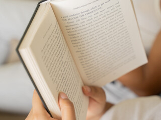 Fototapeta premium Close-up of a woman's hands holding an open book with clearly visible text pages, shot in warm cozy indoor lighting with a soft glowing table lamp in the background, evoking reading and knowledge. 