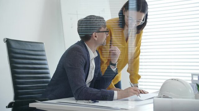 Architects and engineers reviewing blueprints and project plans at a desk, collaborating on design solutions and construction strategy in a modern professional office setting