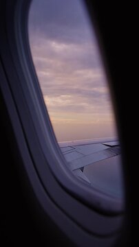 Vertical video. Airplane Window Frames a Peaceful Sunset Sky and Wing Above the Ocean, Air Travel and Freedom
