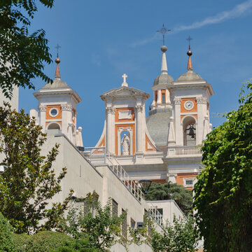 Facade, bell towers and domes of San Francisco de Borja Church framed by trees under a blue sky in Madrid, Spain.