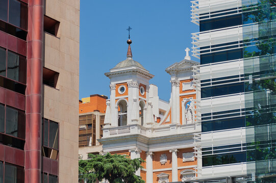 Facade and bell tower of San Francisco de Borja Church framed between modern office buildings under a clear blue sky in Madrid, Spain.