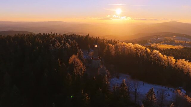 Stepanka Lookout Tower is located in the Jizera Mountains. The sun sets over the trees, creating a warm glow in winter and autumn. Explore this natural beauty during your hike.