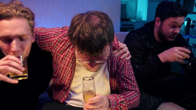 Drunk friends celebrate holiday with alcohol drinks. Playful group enjoys shots and laughter together. Three caucasian young men toast on sofa in cheerful apartment. The problem of alcohol abuse