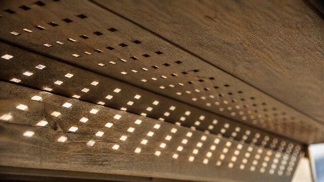 Extreme close-up of wooden soffit with sunlight streaming through holes.
