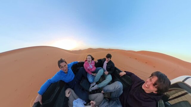 Young adults riding in pickup truck bed across desert dunes at sunset