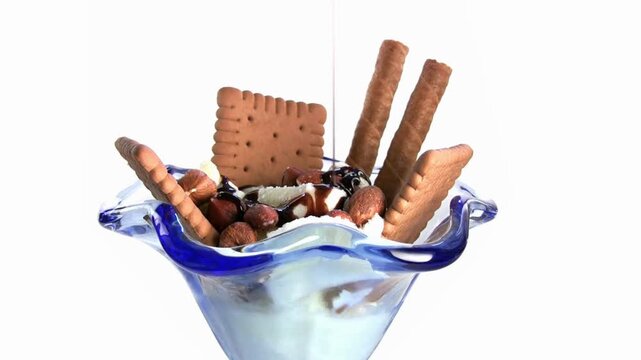 Gourmet vanilla ice cream sundae with chocolate biscuits and wafer rolls, delicious dairy dessert in blue glass bowl, sweet treat with hazelnut toppings