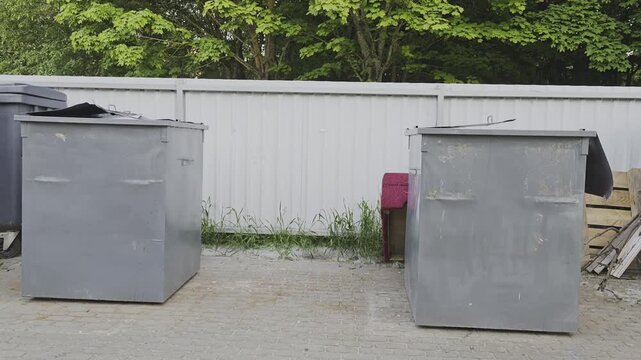 Big metal trash containers standing on pavement. A dirty, grey industrial bin for waste collection and recycling outdoors in an urban area